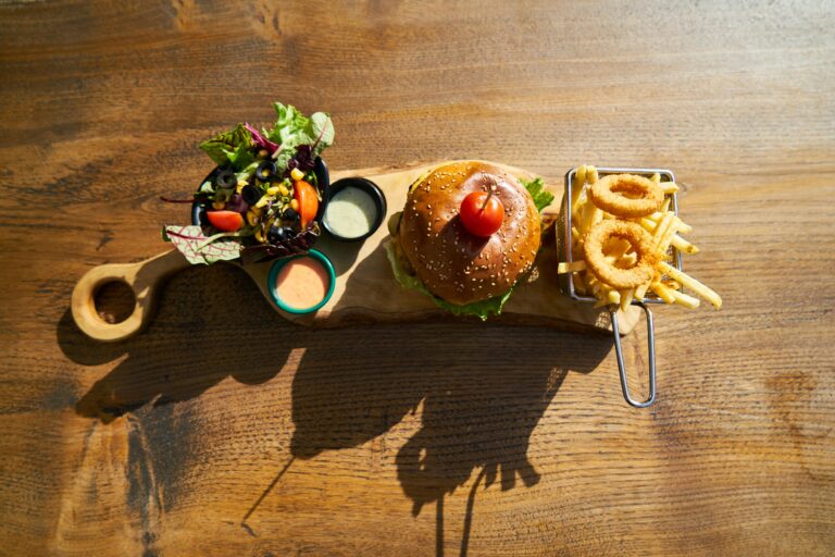 Delicious gourmet burger served with salad, fries, and onion rings on a rustic wooden board.