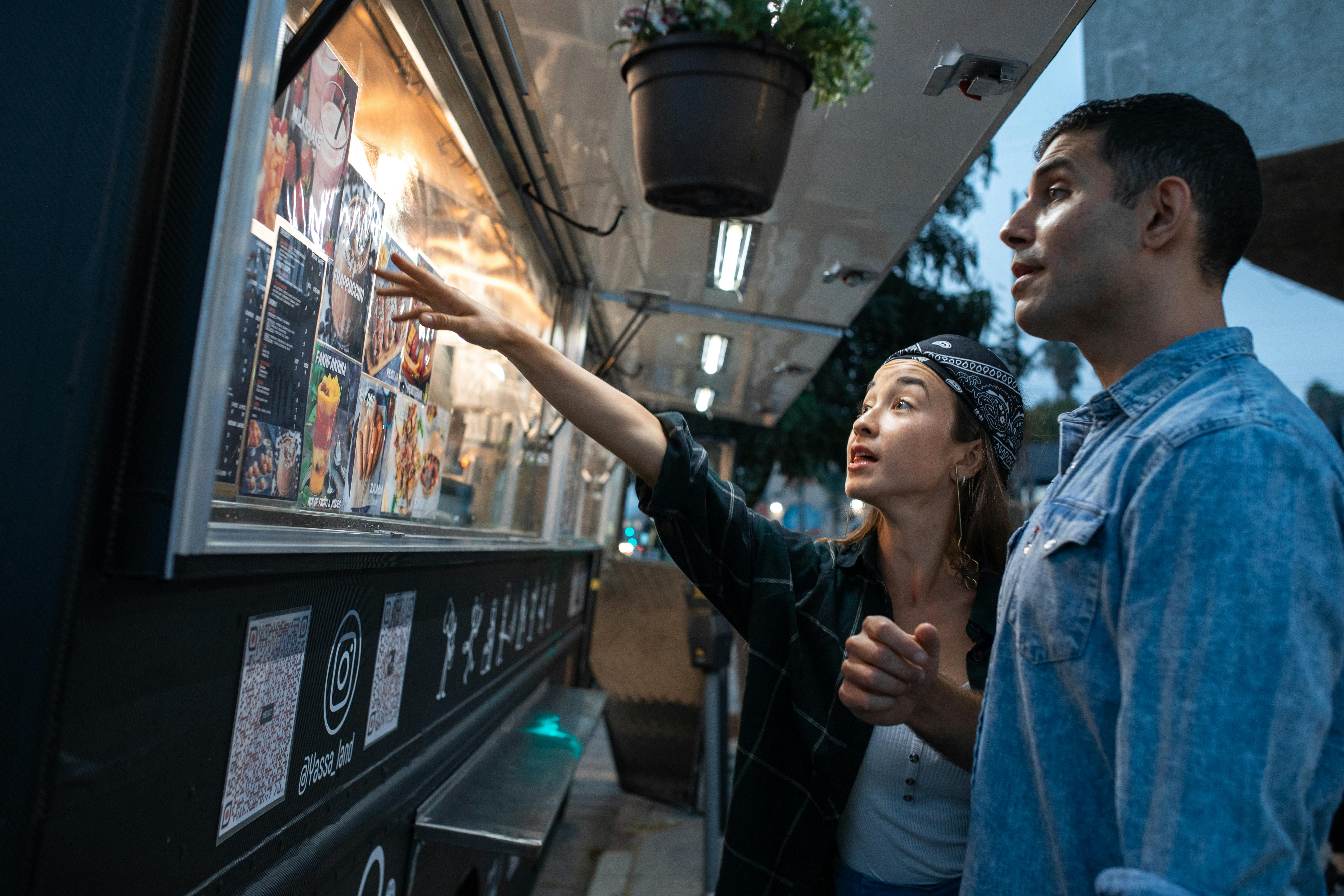 A couple choosing food from a vibrant street food truck menu during the evening.